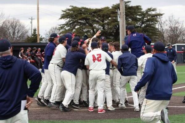Shenandoah University players and coaches celebrate a walk-off grand slam at home plate.